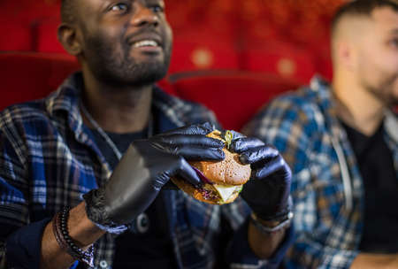 Friends watching a movie in the cinema and eat burgers. People sit in the armchairs of the cinema and look at the screenの写真素材