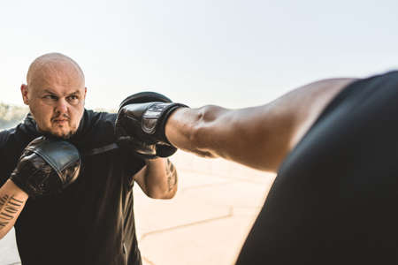 Two men exercising and fighting in outside. Boxer in gloves is training with a coachの写真素材