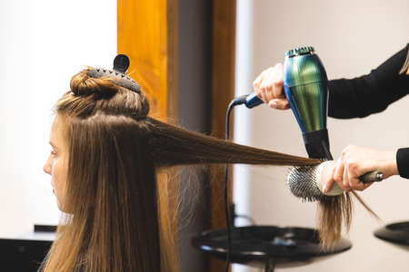 Master woman hairdresser dries the girls hair with a hairdryer and combs after washing in the beauty...