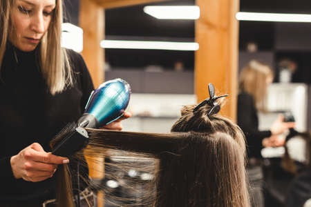 Master woman hairdresser dries the girls hair with a hairdryer after washing in a beauty salon.の写真素材