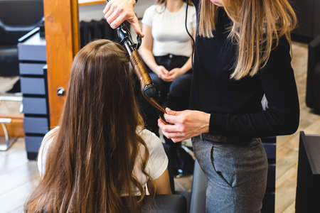 Master woman hairdresser gently curls hair curling girl in a beauty salon. Hair stylingの写真素材