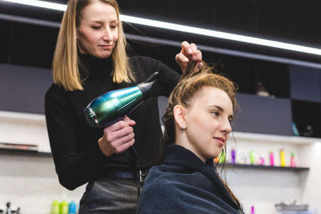 Master woman hairdresser dries the girls hair with a hairdryer after washing in a beauty salon.