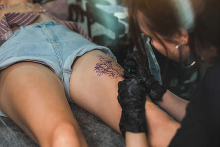 Professional female tattoo artist makes a tattoo in the studio, close-up. Dark photographyの写真素材