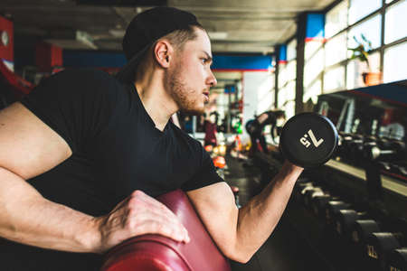 Portrait of a muscular man performs exercises in the gym. Strength training with dumbbells