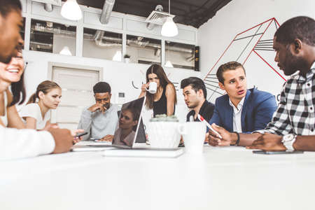A team of young office workers, businessmen with laptop working at the table, communicating together...
