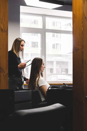Master woman hairdresser gently curls hair curling girl in a beauty salon. Hair stylingの写真素材