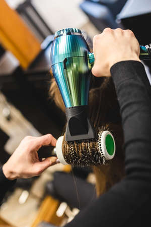 Master woman hairdresser dries the girls hair with a hairdryer and combs after washing in the beauty salon.の写真素材