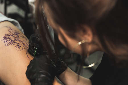 drawing of a tattoo on the leg close-up. Woman tattoo artist makes a drawing with a special machine in an art studioの写真素材