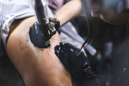 Woman tattoo artist doing tattoo in studio, making tattoo on body. closeupの写真素材