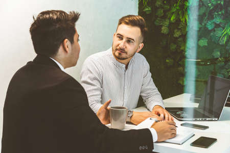 Young office worker sitting at desk, using computer. Two business man talking