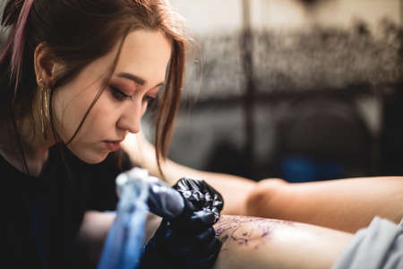Professional female tattoo artist makes a tattoo in the studio, close-up. Dark photography