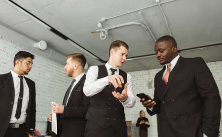 Dialogue of two men with with smartphones young businessmen in suits working and communicating...