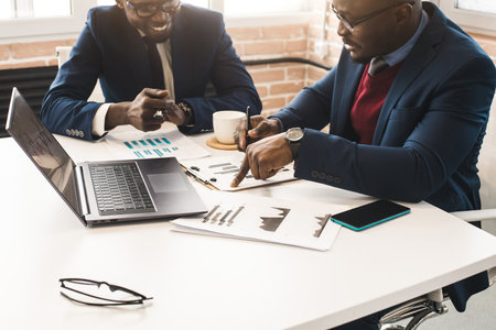 Two dark-skinned partners of an African American businessman in a meeting work on a laptop in the office. Affordable private courses and distance learning. New opportunities onlineの写真素材