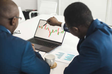 Two African American business partners are working on a laptop studying stock market charts and technical analysis. Training in investment and analysis of macroeconomic and financial indicatorsの写真素材