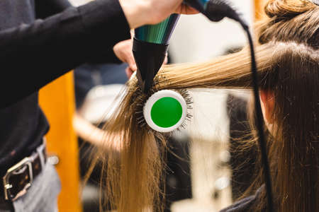Master woman hairdresser dries the girls hair with a hairdryer and combs after washing in the beauty salon.の写真素材