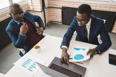 Two dark-skinned partners of an African American businessman in a meeting work on a laptop in the...