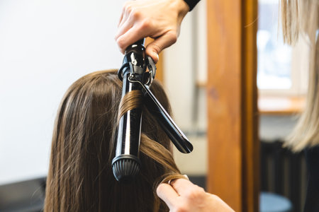 Master woman hairdresser gently curls hair curling girl in a beauty salon. Hair stylingの写真素材