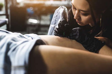 Professional female tattoo artist makes a tattoo in the studio, close-up. Dark photographyの写真素材