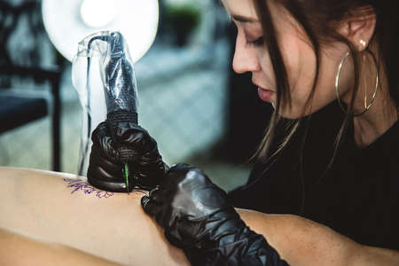 drawing of a tattoo on the leg close-up. Woman tattoo artist makes a drawing with a special machine in an art studioの写真素材