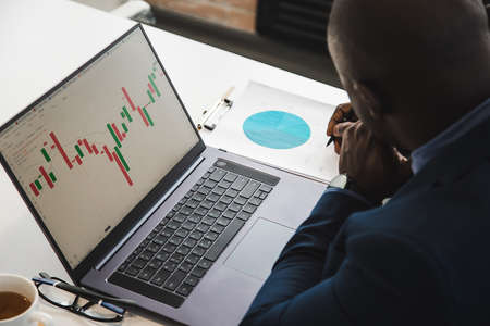 African American men in a business suit are working on a laptop studying stock market charts and technical analysis.の写真素材