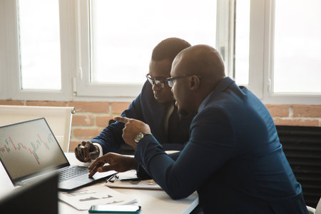 Two dark-skinned partners of an African American businessman in a meeting work on a laptop in the office. Affordable private courses and distance learning. New opportunities onlineの写真素材