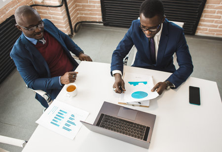 Two African American business partners are working on a laptop studying stock market charts and technical analysis. Training in investment and analysis of macroeconomic and financial indicatorsの写真素材