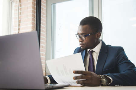 A black African American businessman in a business suit works at a laptop. Analytics and work onlineの写真素材