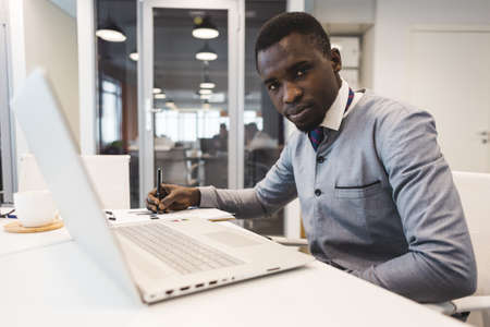 A black African American businessman in a national ethnic business suit works at a laptop. Analytics and work onlineの写真素材