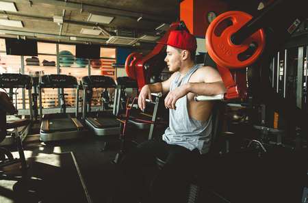 Muscular young male athlete is resting between exercises. Strength training in the gym on the simulatorの写真素材