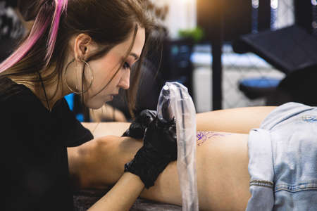 Woman tattoo artist doing tattoo in studio, making tattoo on body. closeupの写真素材