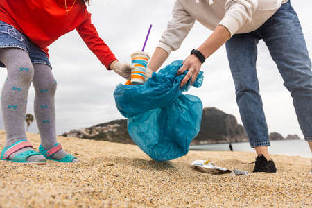 Asian woman picking bottle into plastic bag black for cleaning the beach in morning time, Volunteer...