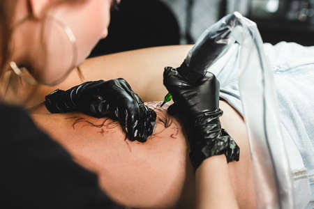 Professional female tattoo artist makes a tattoo in the studio, close-up. Dark photographyの写真素材