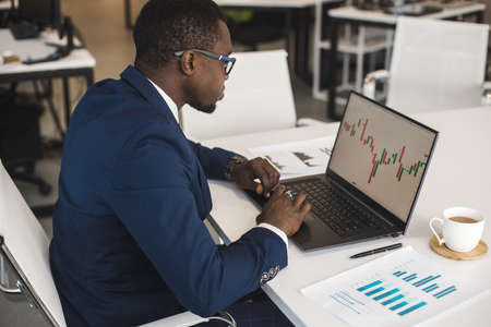 African American men in a business suit are working on a laptop studying stock market charts and technical analysis.の写真素材