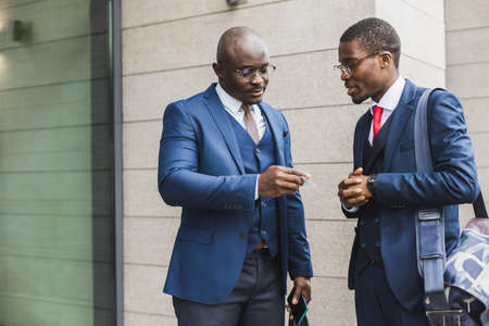 Portrait of two black African American businessman in suits exchanging business cards and contacts outdoors.の写真素材