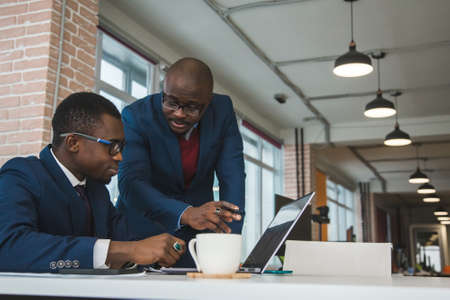 Two dark-skinned partners of an African American businessman in a meeting work on a laptop in the office. Affordable private courses and distance learning. New opportunities onlineの写真素材