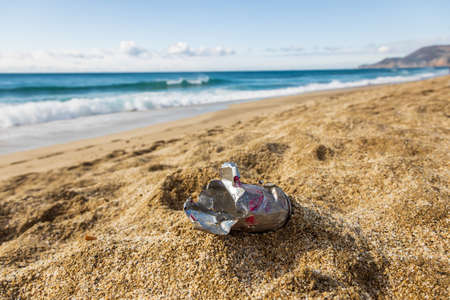 An old tin can washed up by the sea on a sandy shore. Mankind pollutes natureの写真素材