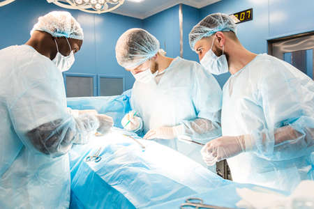 An international team of doctors performs a complex surgical operation on a patient under anesthesia. Modern operating room and experienced surgeons save livesの写真素材