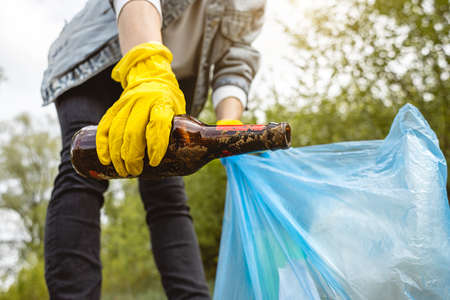 A woman picks up an abandoned glass bottle in the forest. Environmental garbage pollution