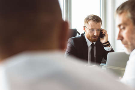 A group of company employees sits at a table in a meeting room. A team of young businessmen working and communicating together in an office. Corporate business team and manager in a meetingの写真素材