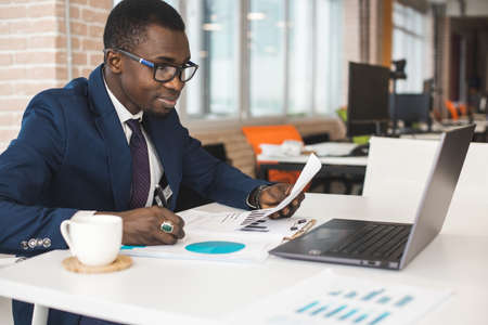 Portrait of an African American in the office. Black man in a business suit working on a laptopの写真素材
