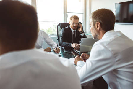 A group of company employees sits at a table in a meeting room. A team of young businessmen working...