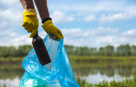 A woman picks up an abandoned glass bottle in the forest. Environmental garbage pollutionの写真素材