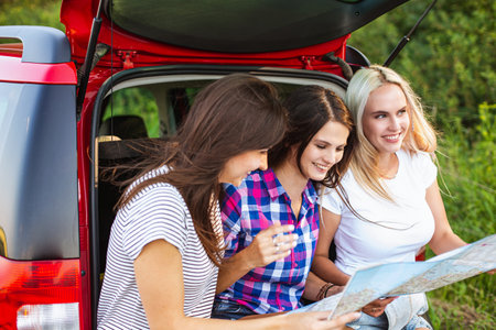Young pretty women friends travel by car. Summer holidays and active recreation. Positive emotions from the adventure. The girls are looking at the mapの写真素材