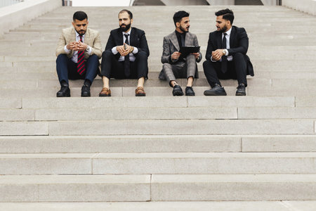 Business people outdoor meeting. A company of male businessmen in suits are sitting on the steps of the stairs. Working break. Teamwork and brainstorming. Successful teamworkの写真素材