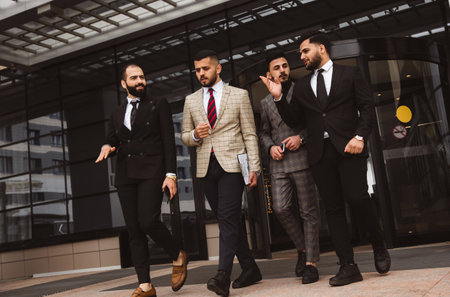 Business people outdoor meeting, A group of male businessmen in suits exit the front door of a glass building. Working break. Teamwork and brainstorming. Successful teamworkの写真素材