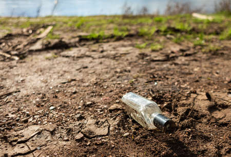 Abandoned garbage in nature. Environmental damage caused by garbage pollution. Left glass bottle among the grass against the background of the riverの写真素材