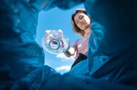 A woman throws a plastic bottle into the trash. Close-up from inside the trash canの写真素材