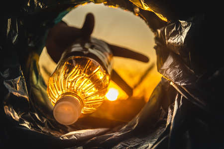 Close-up of a hand throwing a plastic bottle into the trash can. Close-up of the inside of a garbage can in the rays of the setting sunの写真素材