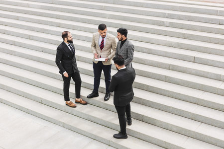 Business people outdoor meeting. A group of men in suits stands against the backdrop of the urban steps of a large staircase. Working break. Teamwork and career advancement. Successful promotionの写真素材
