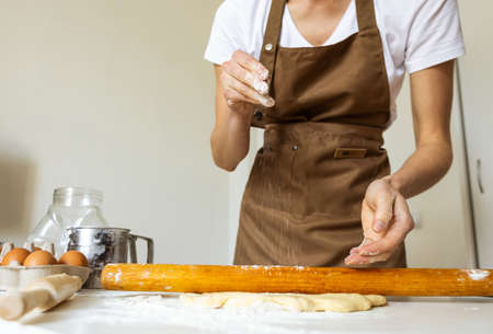 A woman in a special apron cooks at home. Rolling out and preparing dough for baking.の写真素材